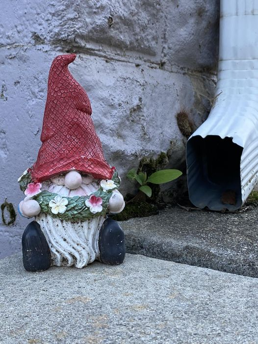 garden gnome near a rain gutter on a sidewalk